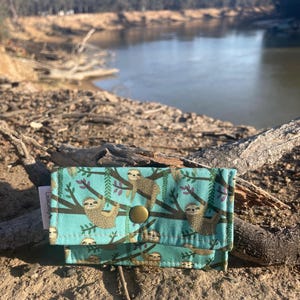 Monedero con forma de perezoso sobre una pequeña cartera para tarjetas de crédito verde de 11 x 8 cm. Se adapta perfectamente al bolsillo delantero de los vaqueros o del bolso. Hecho a mano en Australia.