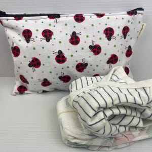Può includere: Una pochette bianca con cerniera con stampa di coccinelle e un body per neonato a righe bianche e nere.
