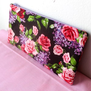Op de afbeelding: Een zwarte rits-tas met een bloemenprint met roze, rode en paarse bloemen op een zwarte achtergrond.