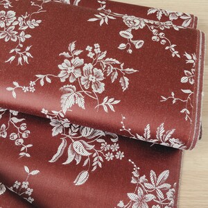 May include: Red fabric with a white floral pattern. The fabric is folded in thirds, showing the pattern repeating.