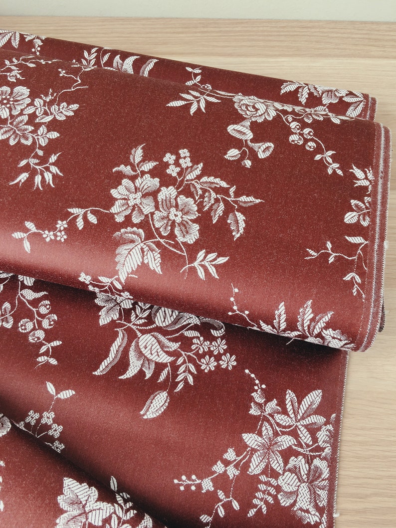 May include: Red fabric with a white floral pattern. The fabric is folded in thirds, showing the pattern repeating.