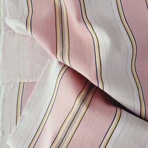 May include: Pink and white striped fabric with thin yellow and brown stripes. The fabric is folded and has a slightly frayed edge.