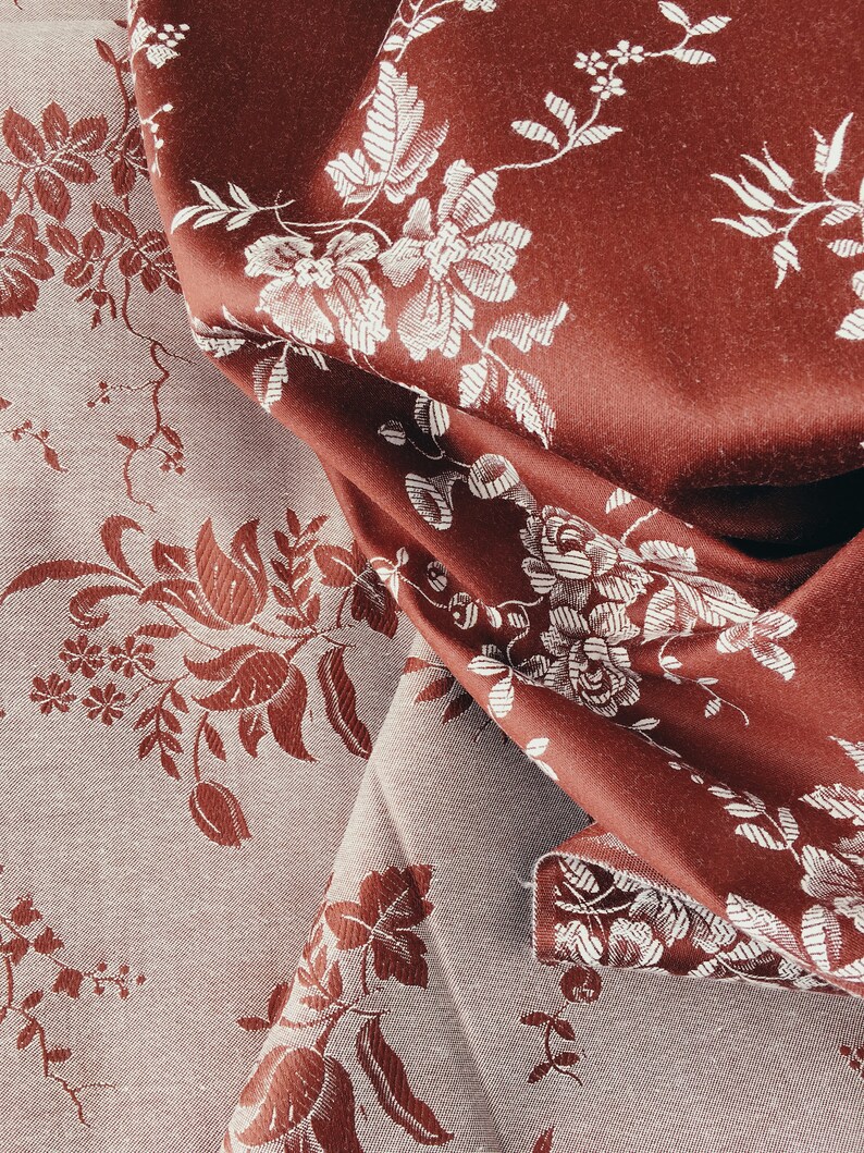 May include: Two pieces of fabric with a floral pattern. One piece is a dark red colour with white flowers and the other is a light grey colour with red flowers.