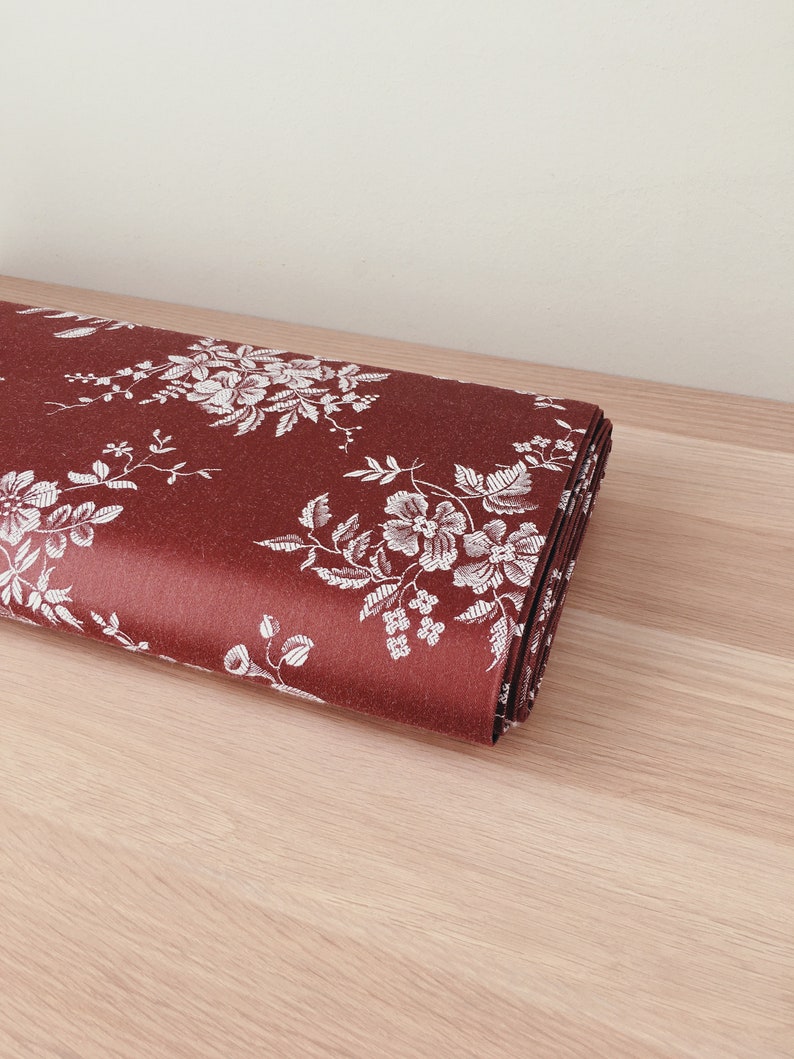 May include: A roll of red fabric with a white floral pattern. The fabric is folded and lying on a light brown wooden surface.