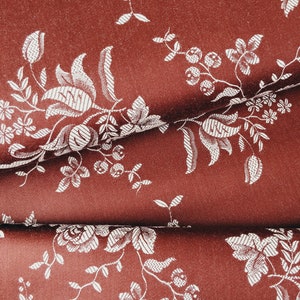 May include: A close-up of a red fabric with a white floral pattern. The fabric is folded in half, showing the pattern on both sides.