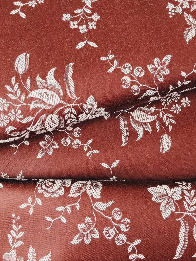 May include: A close-up of a red fabric with a white floral pattern. The fabric is folded in half, showing the pattern on both sides.