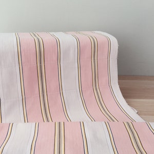 May include: Pink and white striped fabric with thin yellow and brown stripes. The fabric is folded in half and the stripes are running vertically.