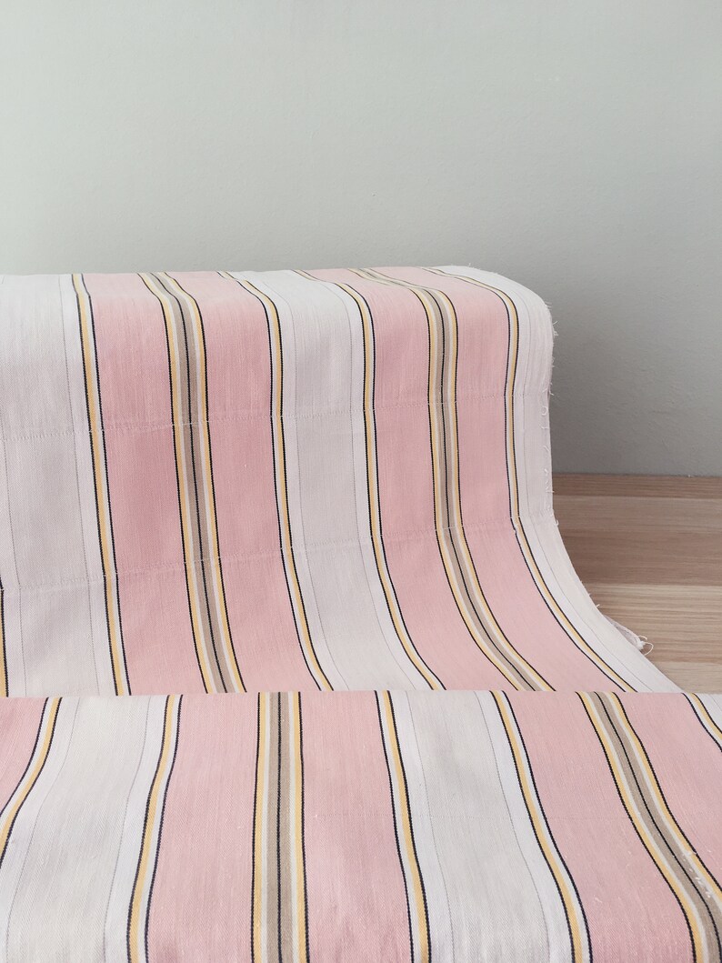 May include: Pink and white striped fabric with thin yellow and brown stripes. The fabric is folded in half and the stripes are running vertically.