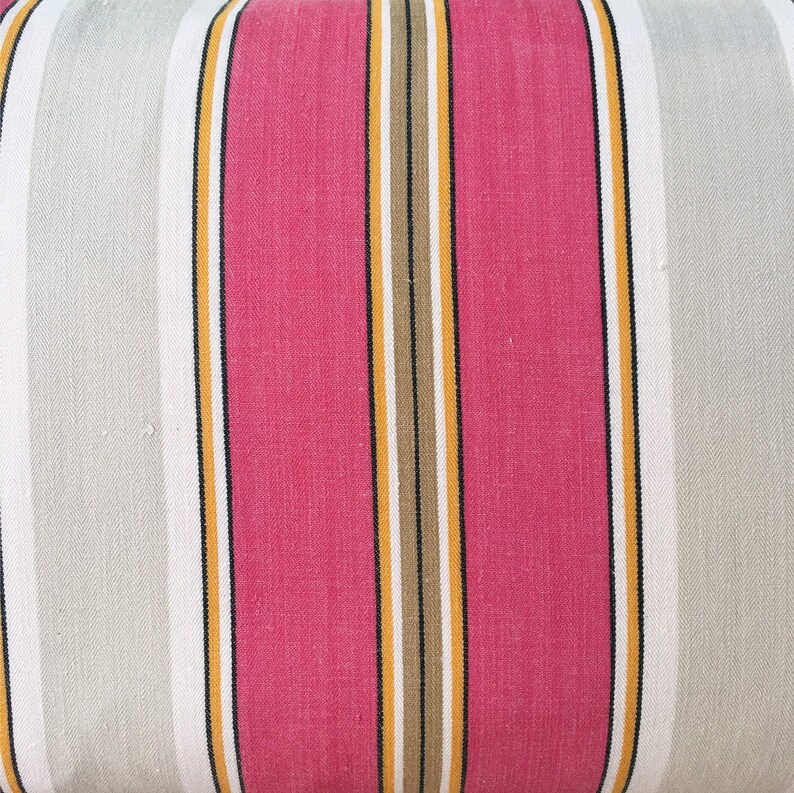 May include: Striped fabric with alternating bands of pink, white, yellow, and brown. The fabric has a woven texture.