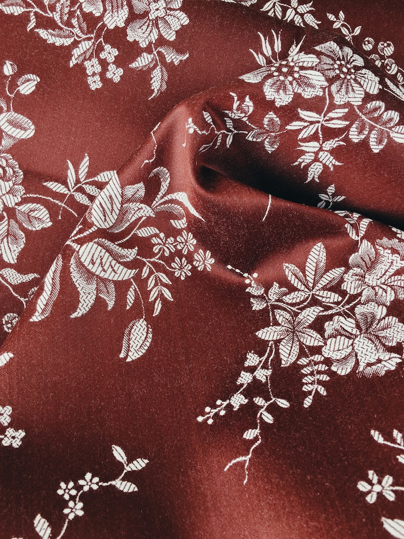 May include: Burgundy fabric with a white floral pattern. The fabric is textured and has a subtle sheen.