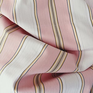 May include: Pink and white striped fabric with thin yellow and brown stripes. The fabric is folded and has a soft, textured appearance.