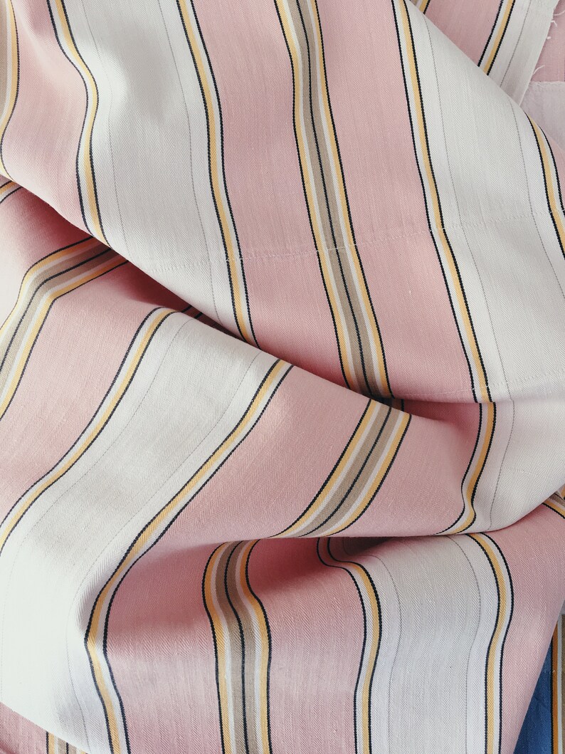 May include: Pink and white striped fabric with thin yellow and brown stripes. The fabric is folded and has a soft, textured appearance.