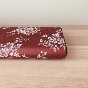 May include: A close-up of a red fabric with a white floral pattern. The fabric is folded in half and is lying on a wooden surface.