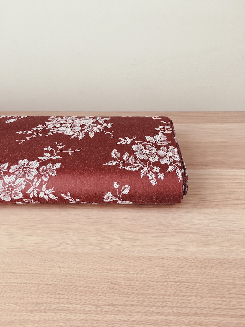 May include: A close-up of a red fabric with a white floral pattern. The fabric is folded in half and is lying on a wooden surface.