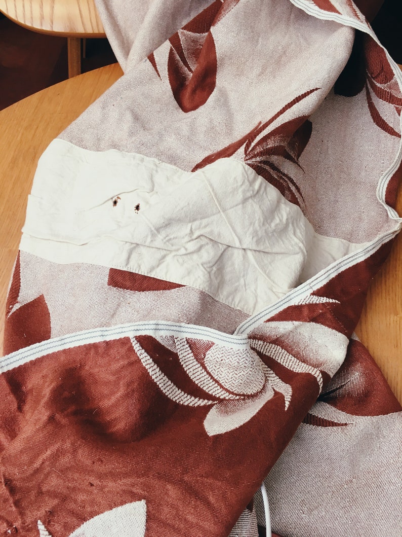 May include: A brown and white woven throw blanket with a floral pattern. The blanket is folded and has a white patch sewn on one side.