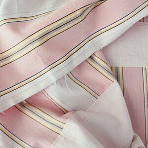 May include: Pink and white striped fabric with thin black and yellow stripes. The fabric is folded and layered, showing the different colors and patterns.