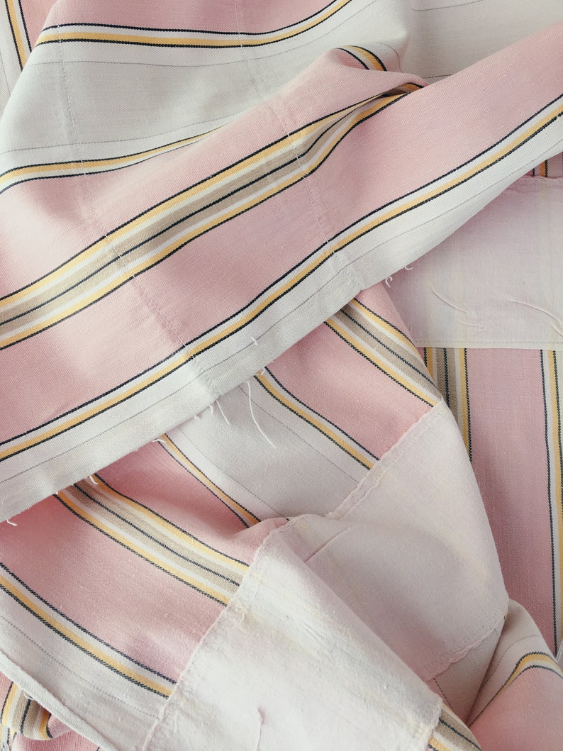 May include: Pink and white striped fabric with thin black and yellow stripes. The fabric is folded and layered, showing the different colors and patterns.