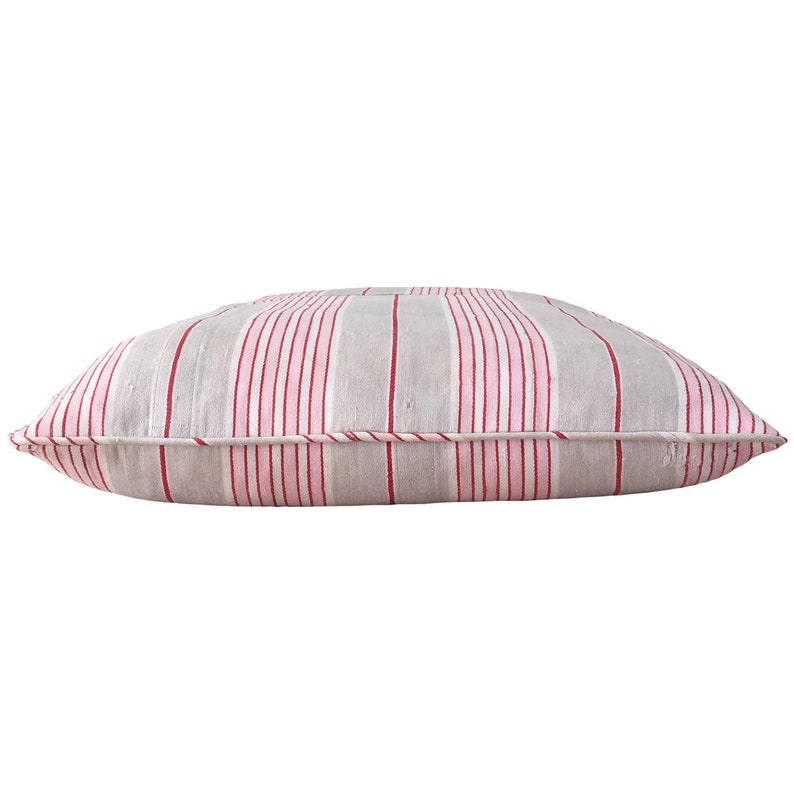May include: A rectangular grey and pink striped cushion with red stripes. The cushion is made of a soft, woven fabric.