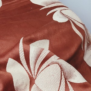 May include: A close-up of a brown fabric with a white floral pattern. The fabric is textured and has a subtle sheen.