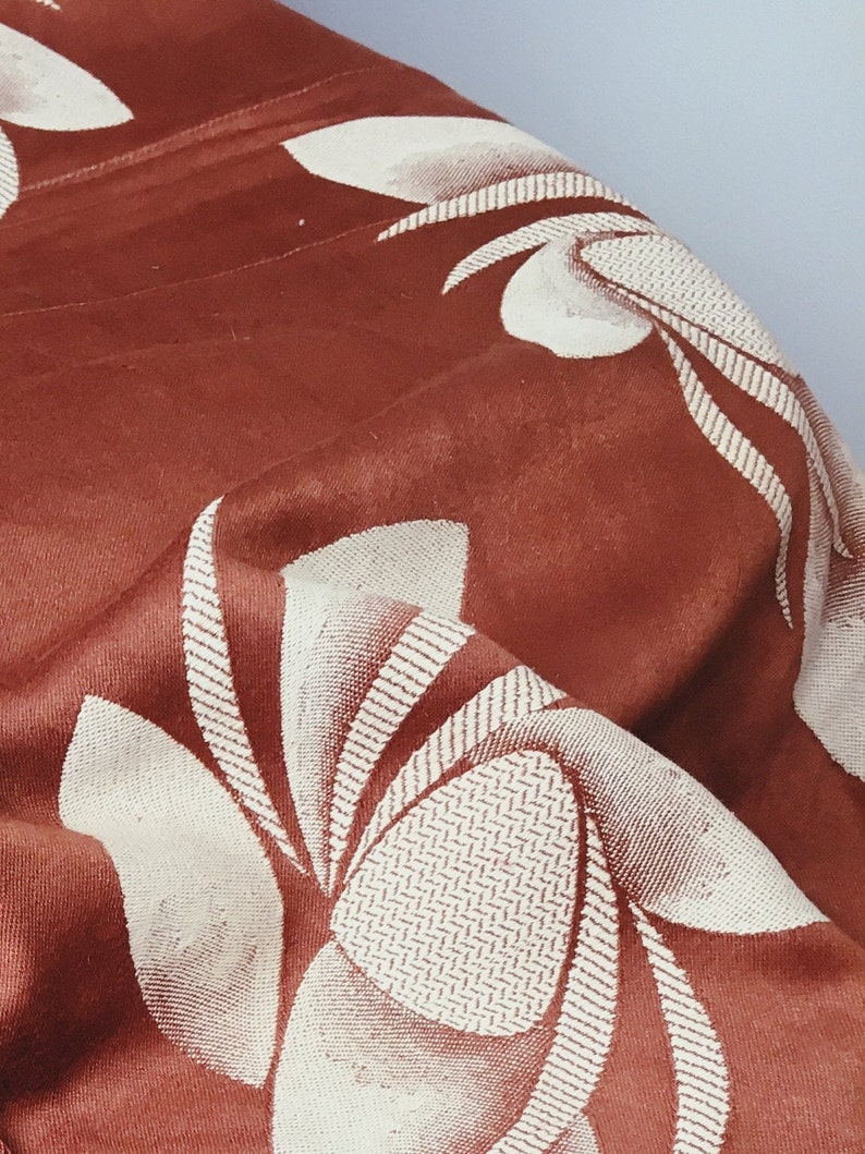 May include: A close-up of a brown fabric with a white floral pattern. The fabric is textured and has a subtle sheen.