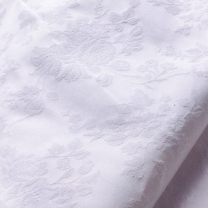 May include: White fabric with a raised floral pattern. The fabric is folded in half and the pattern is visible on both sides.