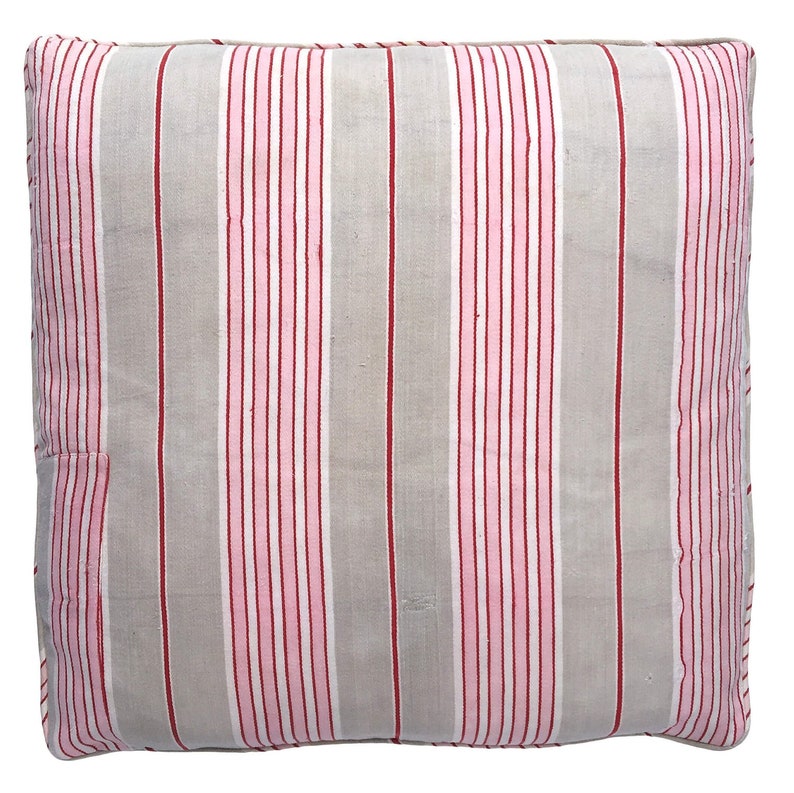 May include: A gray and white striped pillow with pink and red stripes. The pillow is made of a soft, woven fabric.