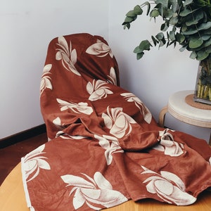 May include: A brown fabric throw blanket with a white floral pattern. The blanket is folded and draped over a chair.