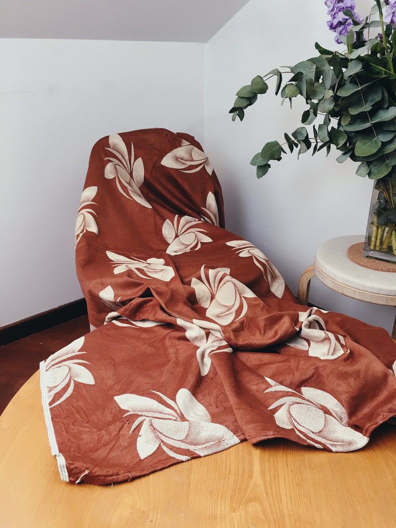 May include: A brown fabric throw blanket with a white floral pattern. The blanket is folded and draped over a chair.