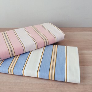 May include: Two pieces of striped fabric folded on a wooden surface. The top fabric is pink and white with thin brown stripes. The bottom fabric is blue and white with thin yellow stripes.