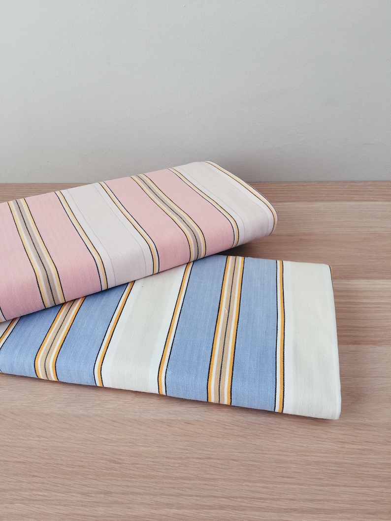 May include: Two pieces of striped fabric folded on a wooden surface. The top fabric is pink and white with thin brown stripes. The bottom fabric is blue and white with thin yellow stripes.