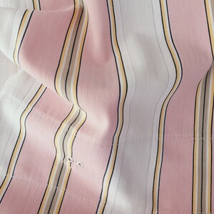 May include: Pink and white striped fabric with thin yellow and brown stripes. The fabric is folded and has a textured surface.