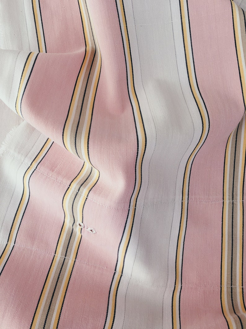 May include: Pink and white striped fabric with thin yellow and brown stripes. The fabric is folded and has a textured surface.