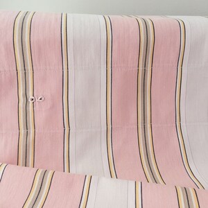 May include: Pink and white striped fabric with thin yellow and brown stripes. The fabric is folded and has a slight wrinkle.
