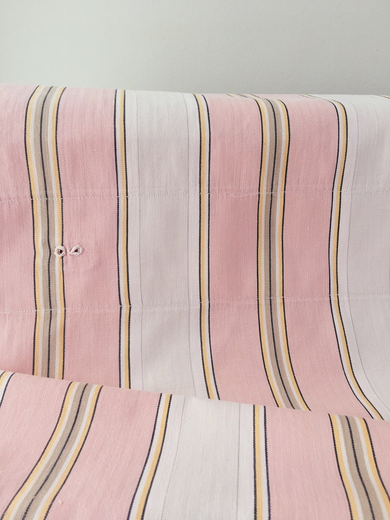 May include: Pink and white striped fabric with thin yellow and brown stripes. The fabric is folded and has a slight wrinkle.