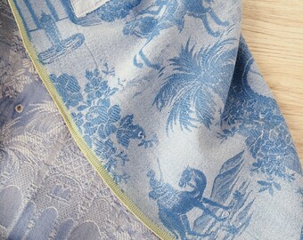 May include: A blue and white fabric with a repeating pattern of stylized flowers, trees, and horses. The fabric has a yellow border.