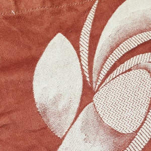 May include: A close-up of a red fabric with a white floral pattern. The fabric has a textured surface and a subtle sheen.