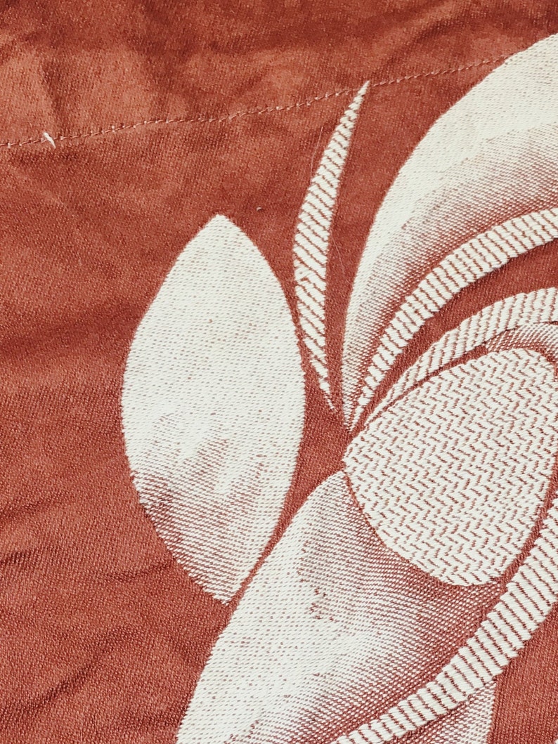 May include: A close-up of a red fabric with a white floral pattern. The fabric has a textured surface and a subtle sheen.