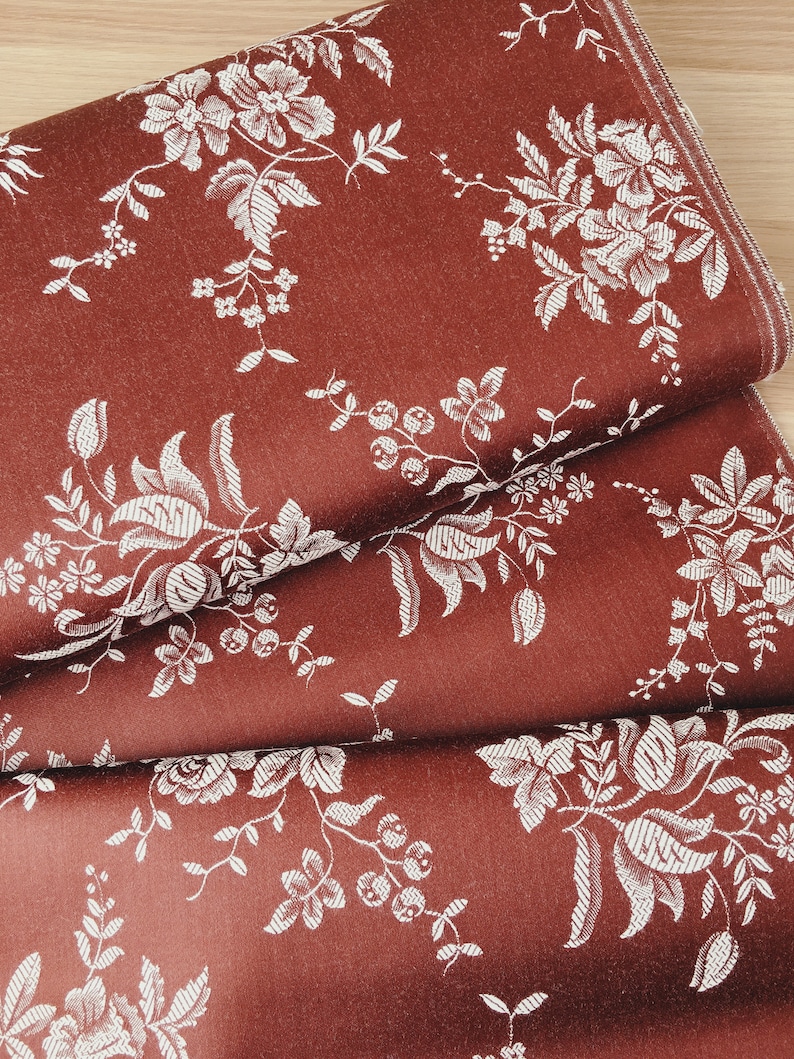 May include: Red fabric with a white floral pattern. The fabric is folded in thirds, showing the pattern from different angles.