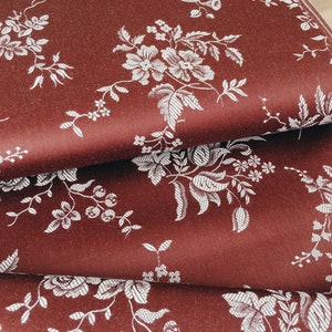 May include: Close-up of a stack of fabric with a burgundy background and a white floral pattern.
