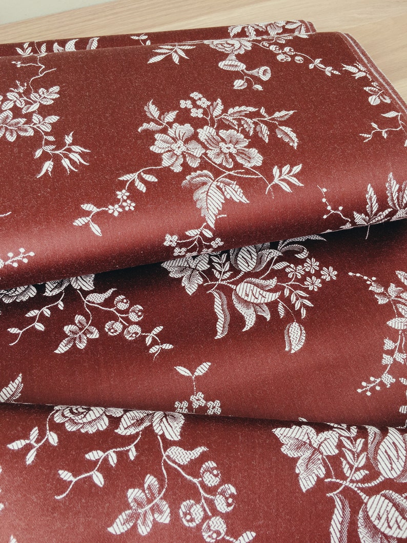 May include: Close-up of a stack of fabric with a burgundy background and a white floral pattern.