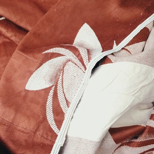 May include: A brown and white patterned throw blanket with a floral design. The blanket is folded and has a textured surface.