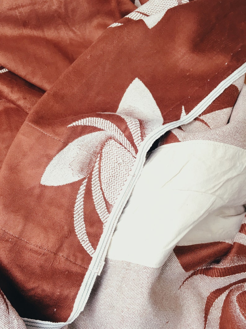 May include: A brown and white patterned throw blanket with a floral design. The blanket is folded and has a textured surface.