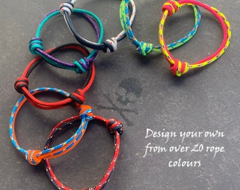 Peut inclure: Plusieurs bracelets en corde colorés, avec des nœuds et des couleurs vives comme le rouge, le bleu et le vert. Le texte de l'image indique : "Design your own from over 20 rope colours."