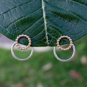 May include: A pair of gold and silver hoop earrings. The earrings are made of two circles, one smaller than the other. The smaller circle is made of gold beads and the larger circle is made of silver.