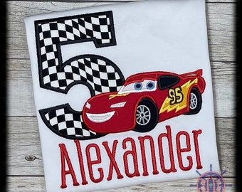 Op de afbeelding: Wit T-shirt met een rode raceauto, nummer 95 en de naam "Alexander" in het rood. Een groot cijfer 5 met een zwart-wit geblokt vlagontwerp staat links. Dit shirt is waarschijnlijk voor een kinderverjaardag.