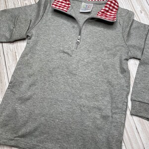 May include: Gray long-sleeve shirt with a red and white gingham collar. The shirt has a zipper closure and the label "LTC" is visible on the collar.