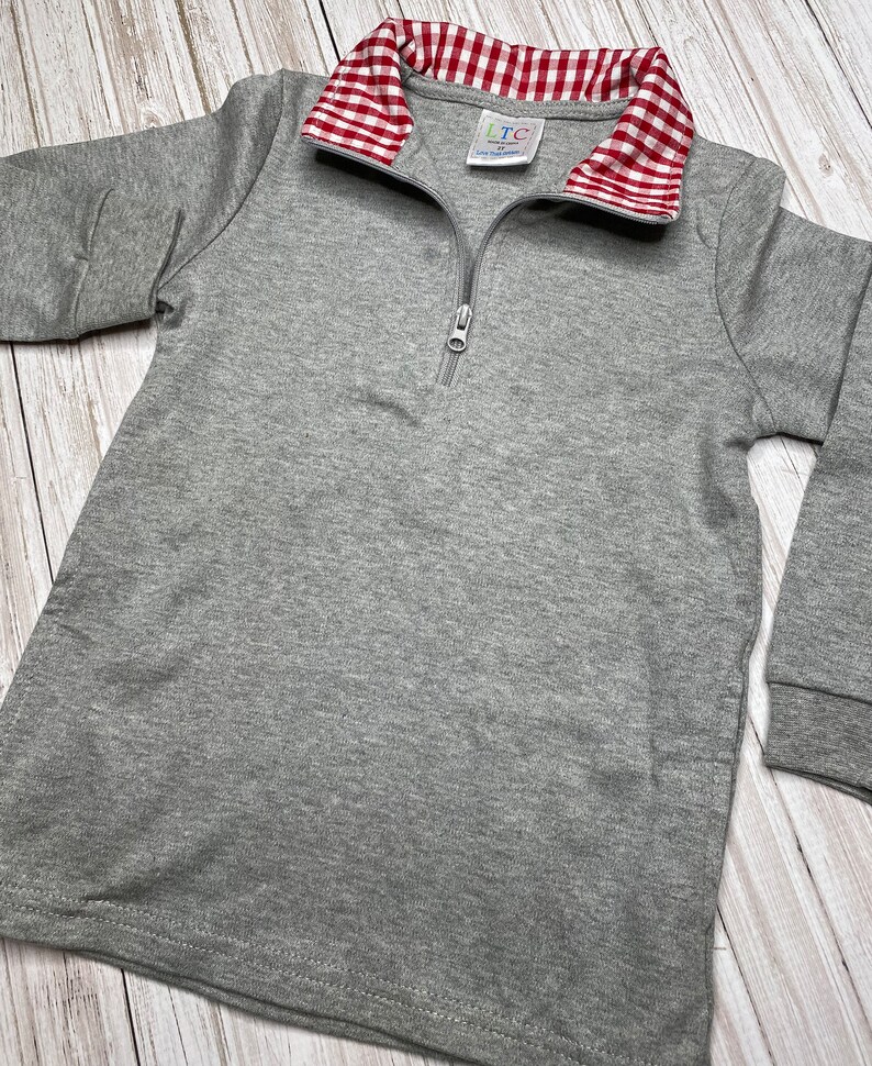 May include: Gray long-sleeve shirt with a red and white gingham collar. The shirt has a zipper closure and the label "LTC" is visible on the collar.