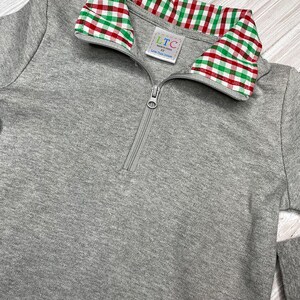 May include: Gray long-sleeve pullover with a red and green plaid collar. The pullover has a zipper closure and a small label that reads "LTC Made in China 3T Love That Cotton".