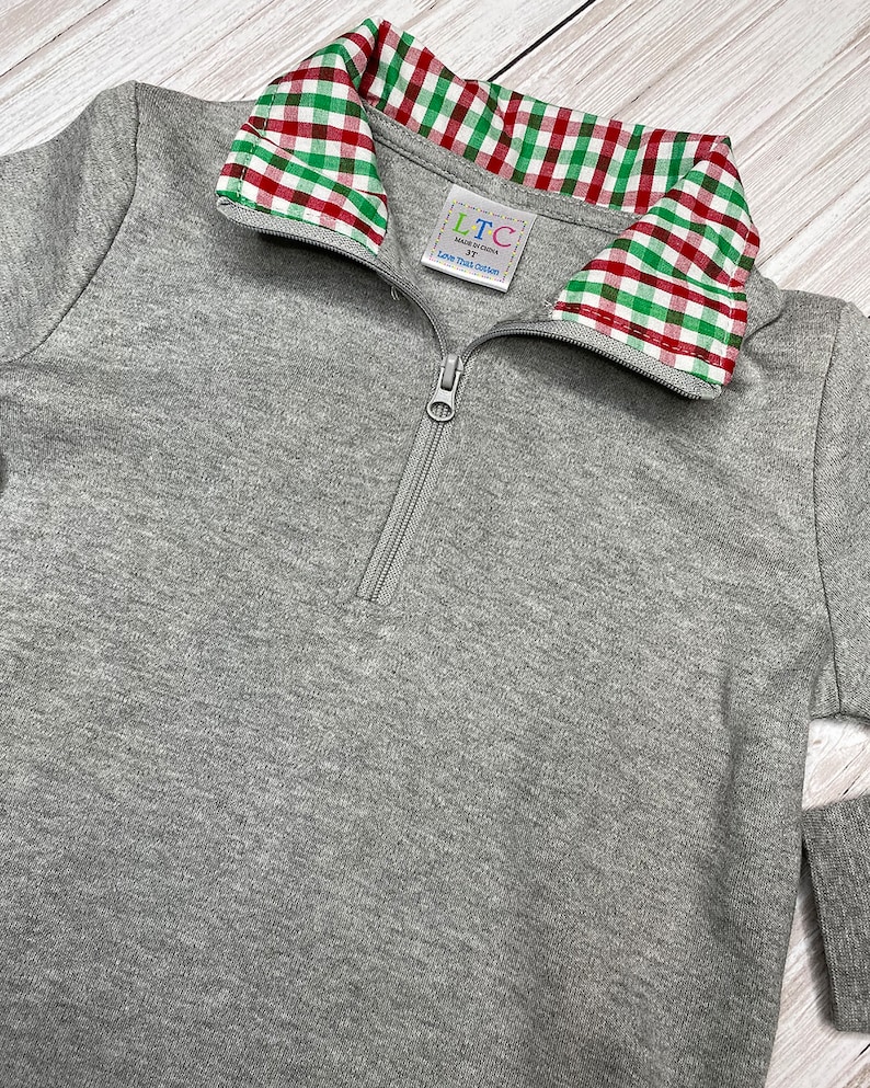 May include: Gray long-sleeve pullover with a red and green plaid collar. The pullover has a zipper closure and a small label that reads "LTC Made in China 3T Love That Cotton".