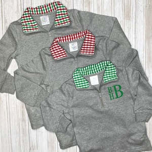 May include: Three gray quarter-zip sweatshirts with different colored gingham collars. The collars are red and green, red and white, and green and white. The bottom sweatshirt has the monogram "BHB" embroidered on the front in green.